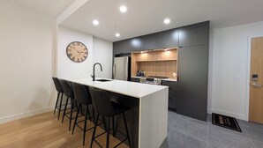 Une cuisine moderne avec un îlot central, des tabourets de bar noirs et une horloge murale.