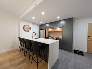 A modern kitchen with a central island, black bar stools, and a wall-mounted clock. - 200-214 - Level 2 - 2BD, 6 people (Beaupré)