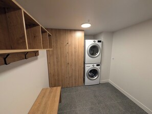 A laundry room with two stacked washing machines, a wooden bench, and a pegboard shelf. - 200-214 - Level 2 - 2BD, 6 people (Beaupré)