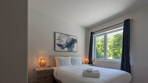 Une chambre à coucher avec un lit, des tables de chevet, une fenêtre avec des rideaux et un tableau au mur.
