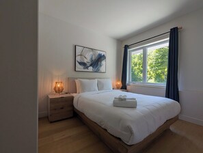 A bedroom with a bed, bedside tables, a window with curtains, and a painting on the wall. - 200-214 - Level 2 - 2BD, 6 people (Beaupré)
