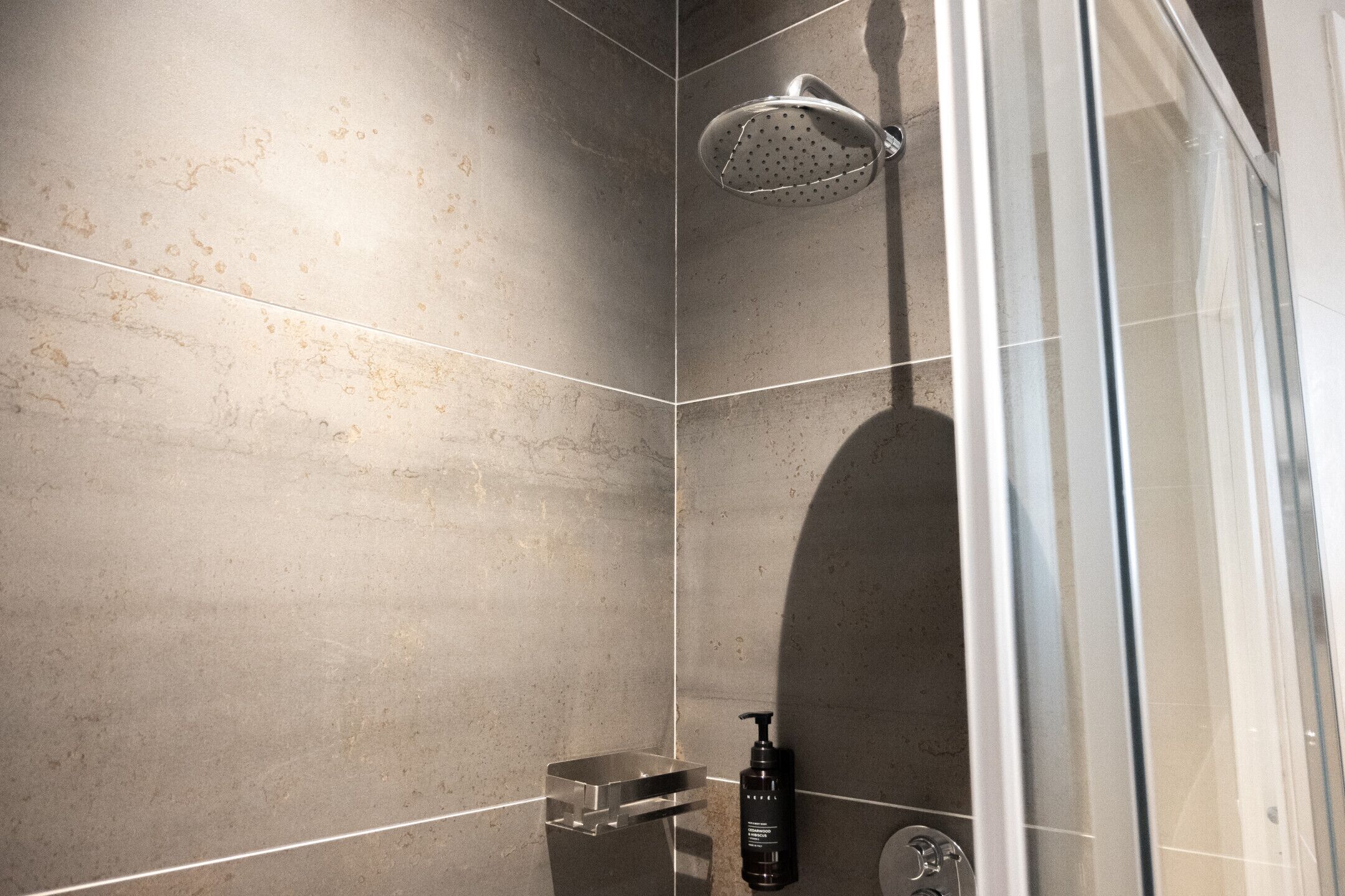 A modern shower with a handheld showerhead, a soap dispenser, and a glass-enclosed shower area.