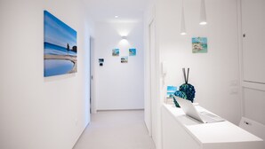 Um corredor com parede branca, um laptop sobre um balcão e uma pintura de uma cena de praia.