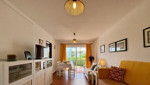 Habitació amb sofà, televisió, taula i cadires, ventilador i vistes per la finestra.