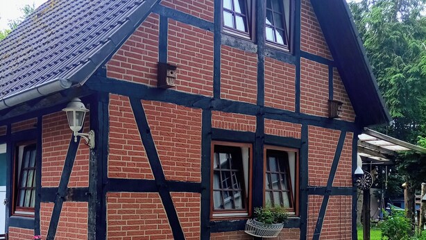 Ett traditionellt hus med korsvirkesfasad, ett brant sadeltak, många fönster och en synlig skorsten.