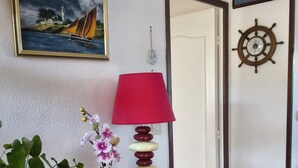 Una taula de fusta amb una làmpada vermella, un vas amb flors i un quadre d'un veler.