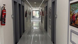 A long, well-lit hallway with doors on both sides, a fire extinguisher on the left, and a framed picture on the right. - Hotel Runway (Vadodara)
