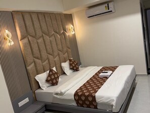 A modern hotel room with a tufted headboard, a bed with white linens and patterned pillows, a brown throw, and an air conditioning unit on the wall. - Hotel Runway (Vadodara)