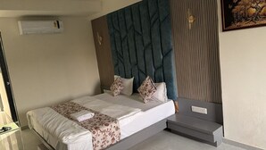 A neatly made bed with a floral bedspread, a headboard with a geometric pattern, and a bedside table with a power outlet. - Hotel Runway (Vadodara)