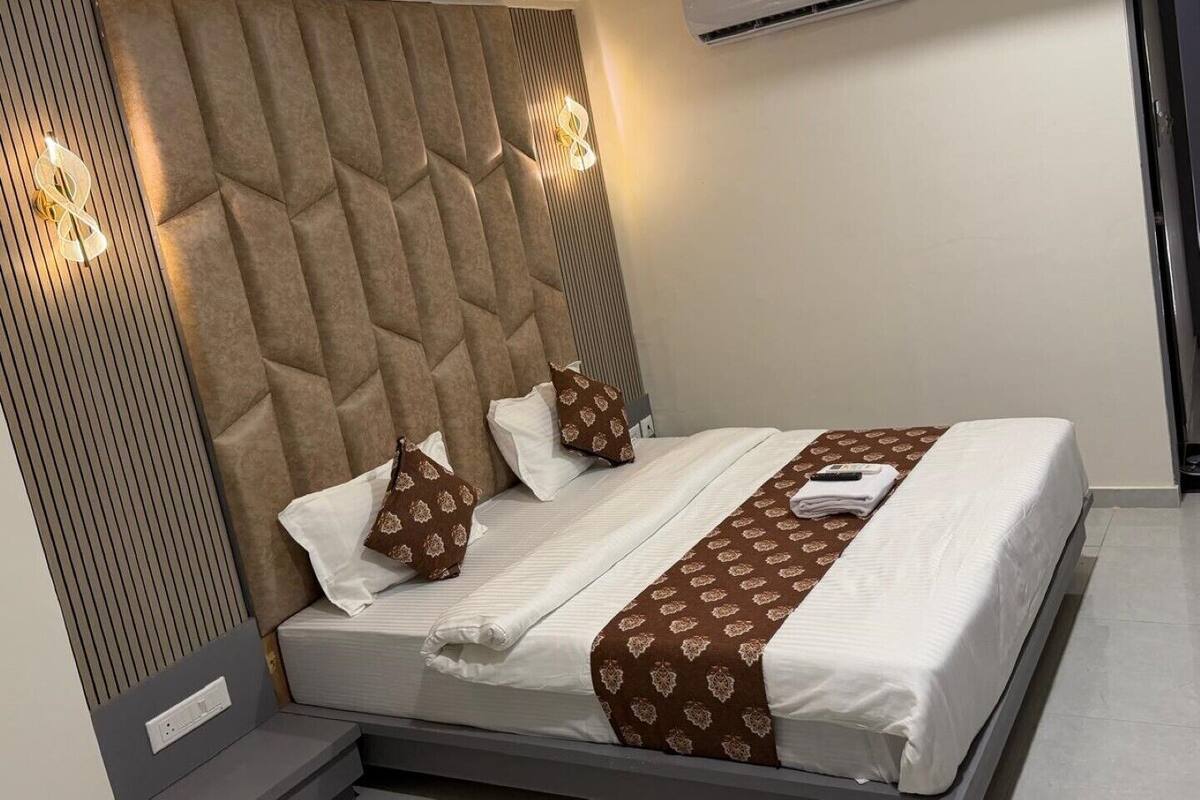 Una habitación de hotel moderna con una cama grande, un cabecero con diseño geométrico, una mesita de noche y un equipo de aire acondicionado.