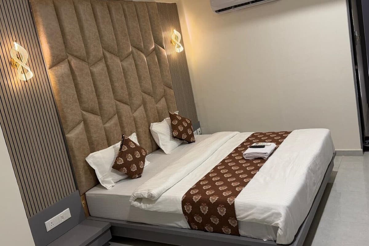 Quarto de hotel moderno com uma cama grande, cabeceira com padrão geométrico, mesa de cabeceira e ar condicionado.