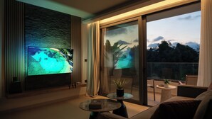 Ett modernt vardagsrum med en stor TV med platt skärm, ett soffbord i glas, en soffa och en balkong med utsikt över omgivningarna.