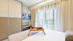 Ett hotellrum med en säng, en tv, ett bricka med mat och ett fönster med gardiner.