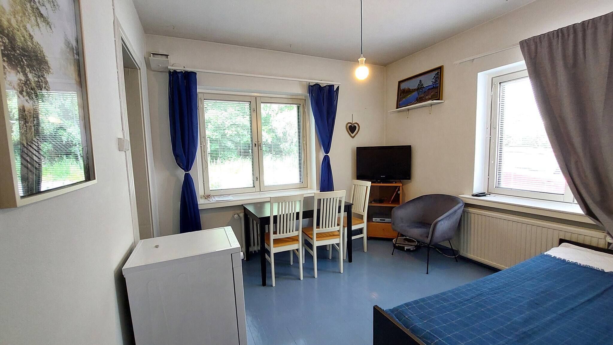 A room with a bed, a desk with chairs, a television, and windows with curtains.