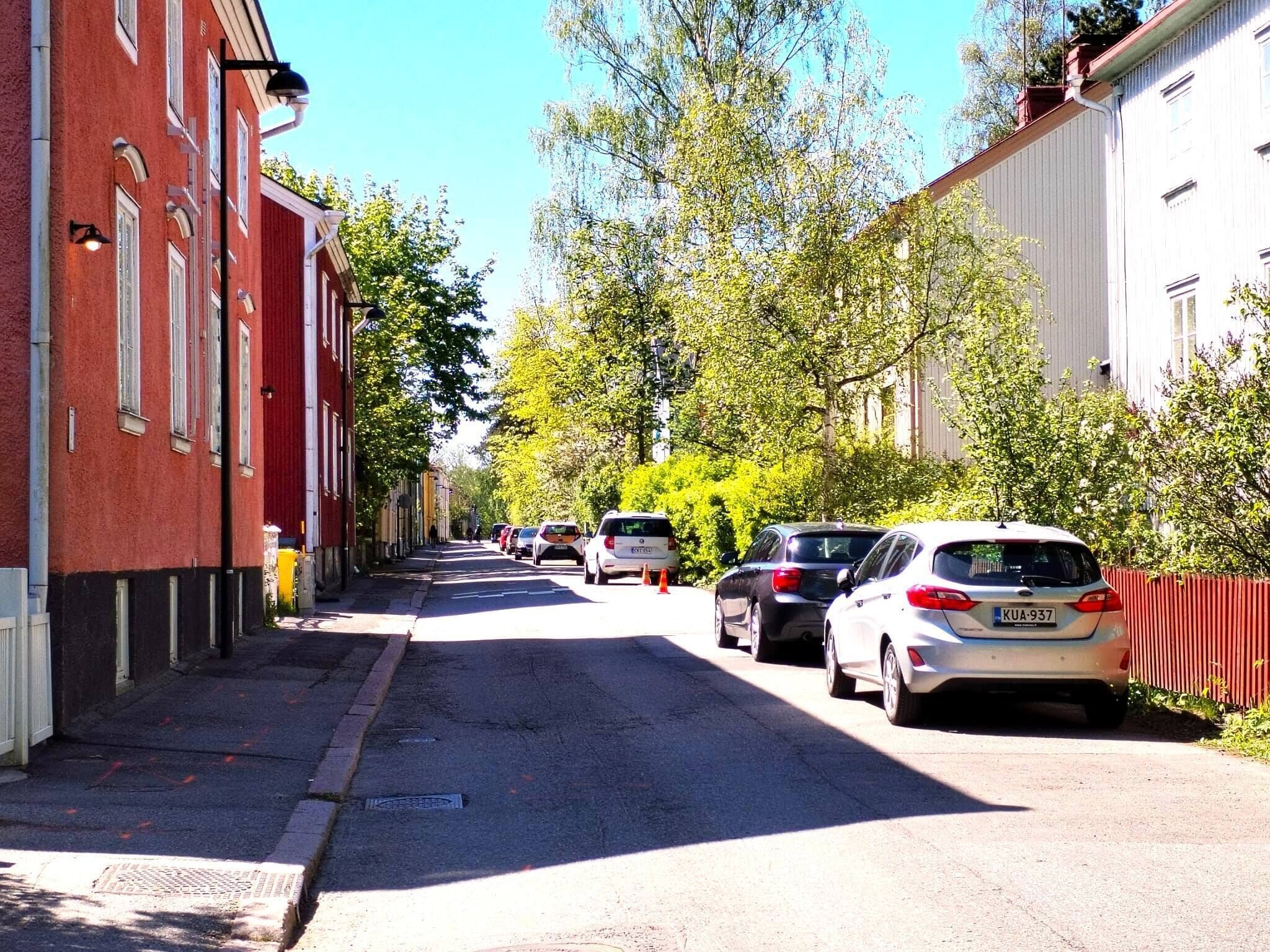 A street lined with parked cars and buildings, a clear sky, and trees.