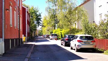 A street lined with parked cars and buildings, a clear sky, and trees.