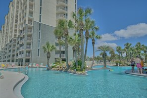 Ein Hotelpoolbereich mit klarem, blauem Wasser, Palmen und einem mehrstöckigen Gebäude mit Balkonen.