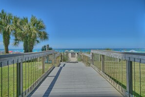 A wooden boardwalk leading to a beach with palm trees and umbrellas.