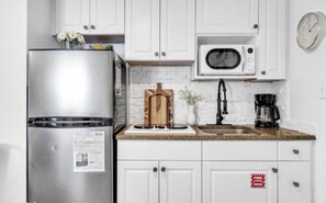Eine Küche mit weißen Schränken, einem Edelstahl-Kühlschrank, einer Mikrowelle, einer Kaffeemaschine und einer Uhr an der Wand.