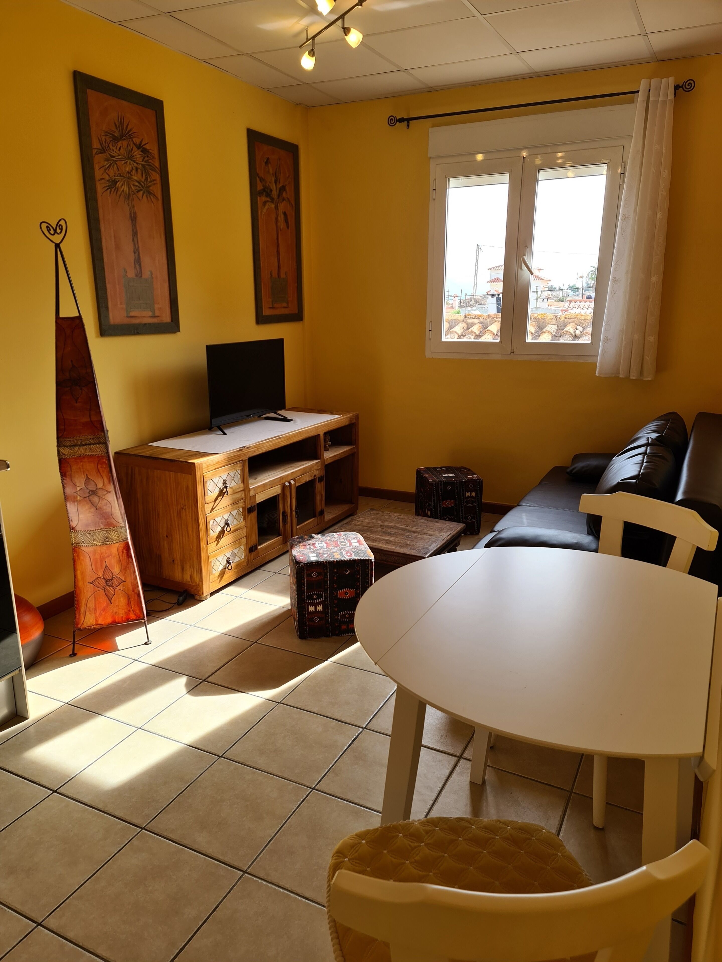 Een woonkamer met een bank, een televisie, een tafel en een raam met gordijnen.