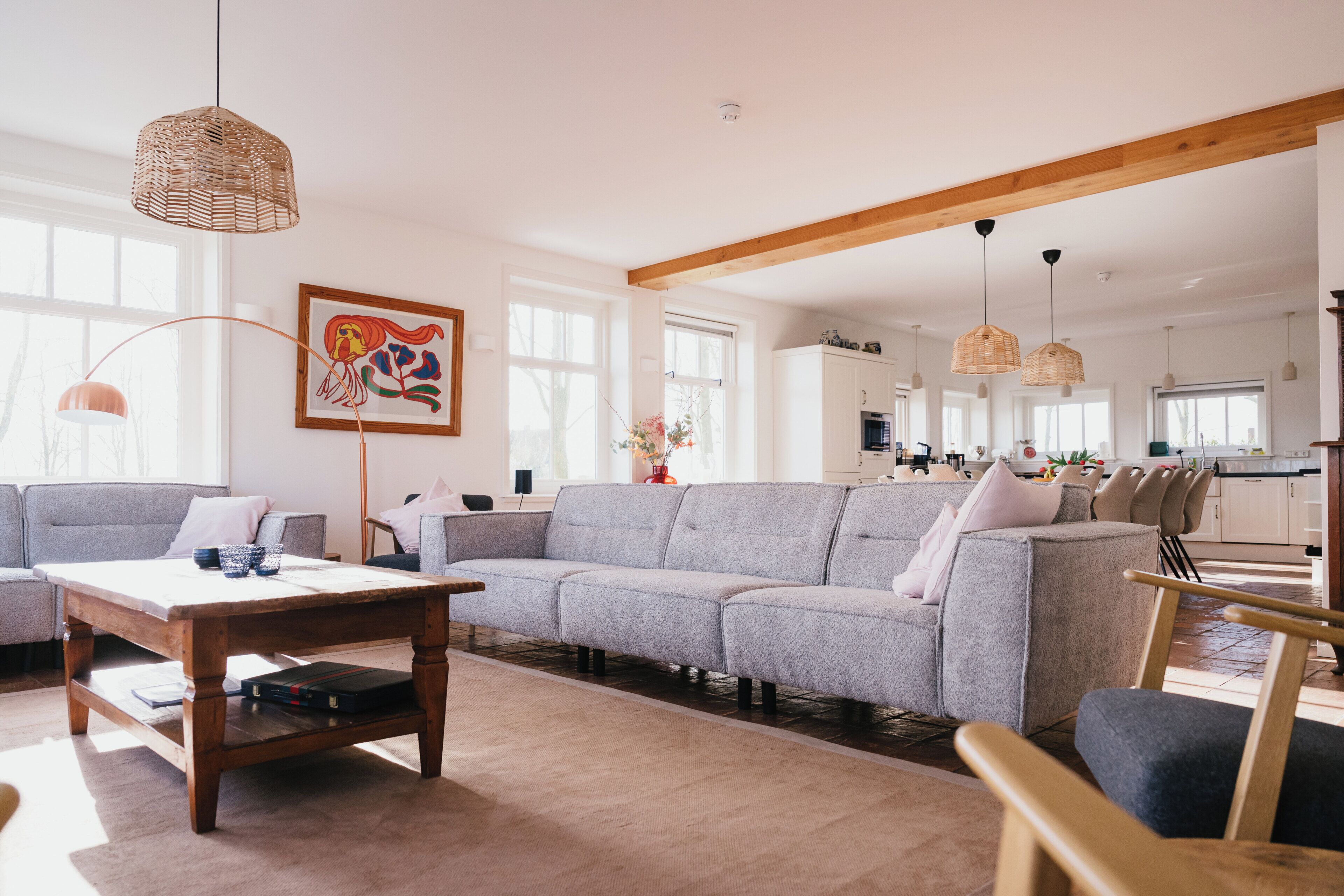 A spacious living room with a grey sectional sofa, a wooden coffee table, and a dining area with a kitchen in the background.