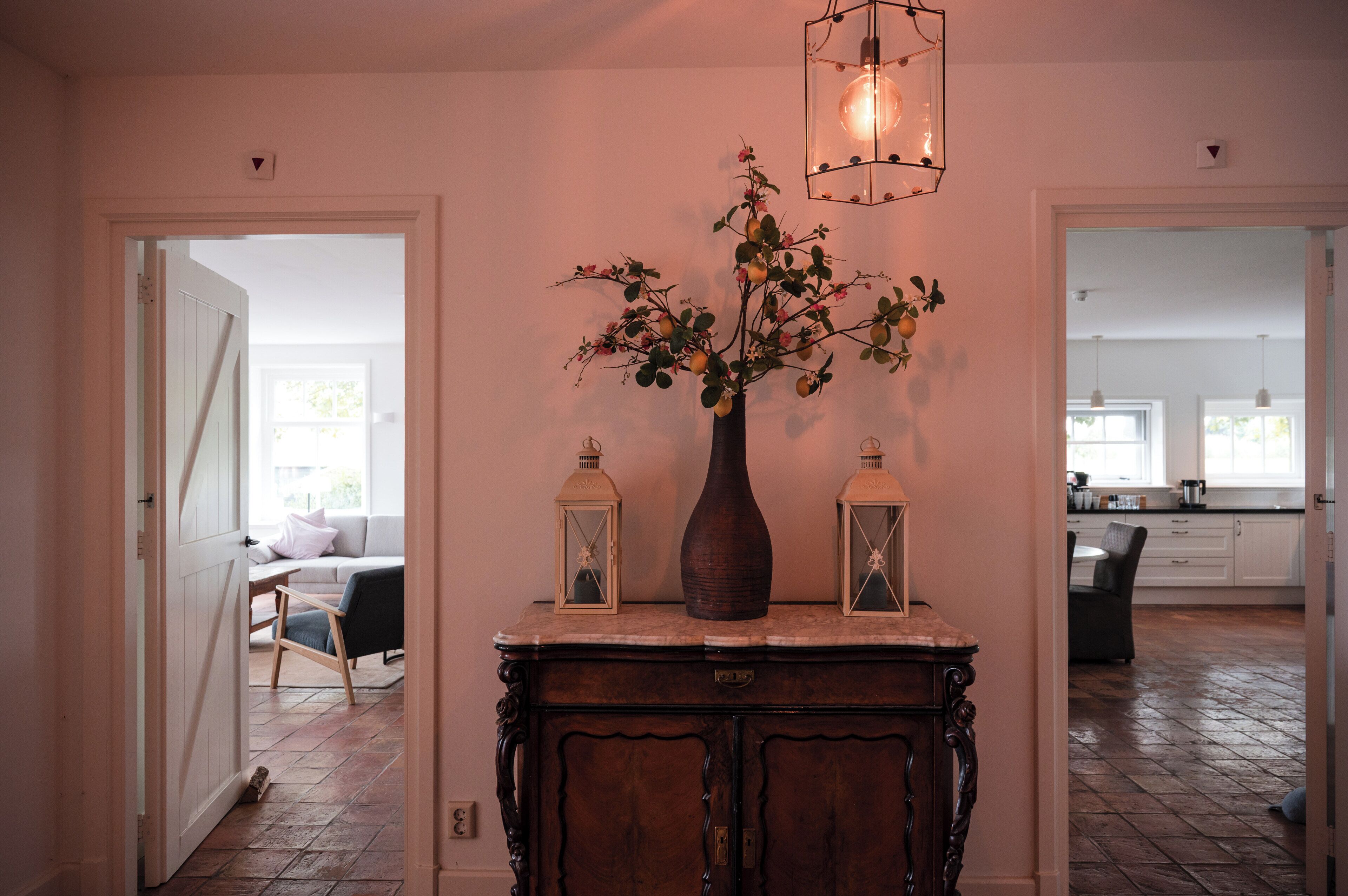 A hallway with a wooden cabinet, a vase with flowers, and two lanterns.