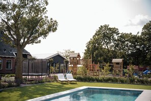 Een achtertuin met een zwembad, een houten speeltoestel en een huis.