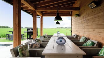 An outdoor covered patio with wooden benches, a table, and a hanging light fixture.