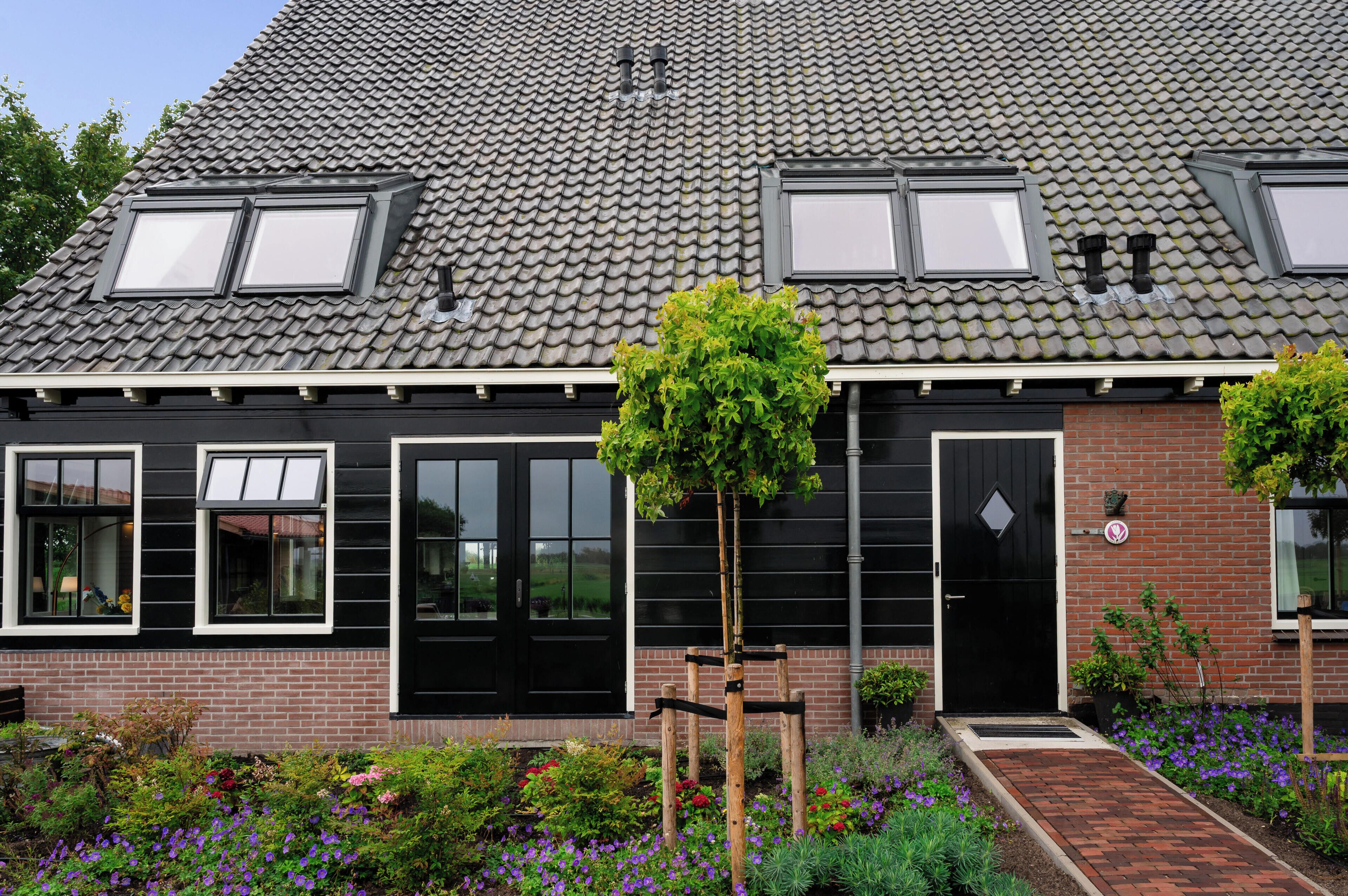 A two-story house with a tiled roof, a black door, and a garden with flowers and a tree.