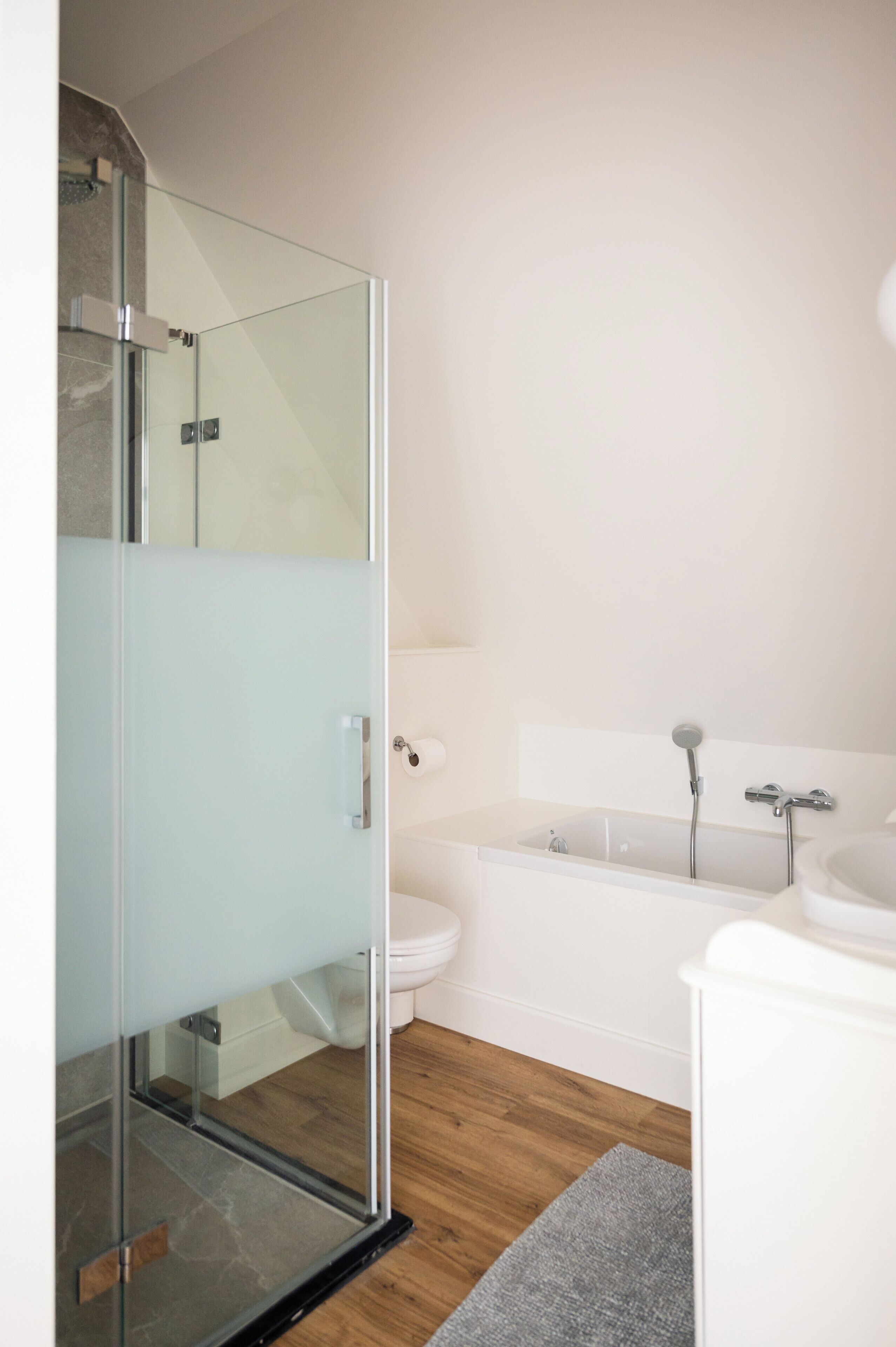 A modern bathroom with a glass shower enclosure, a white toilet, a bathtub, and a sink.