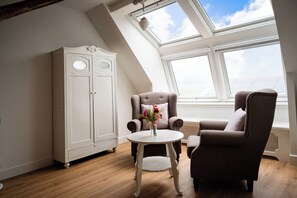 A room with a sloped ceiling, a white wardrobe, two armchairs, a small round table with a vase, and large windows. - Luxurious farm stay with a pool and covered patio in the polder (Grootschermer)