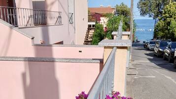 Edifici rosa amb un balcó, un carrer amb cotxes aparcats i vista al mar.