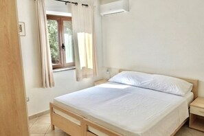 Un dormitorio con cama, ventana con cortinas, mesita de noche y aire acondicionado.