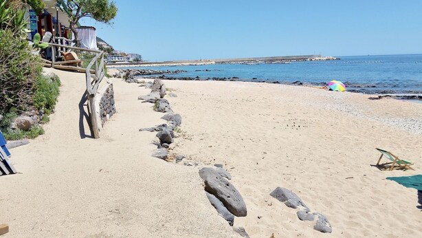 En strand med ett trästaket, en stig som leder till en byggnad och en fri utsikt över havet.