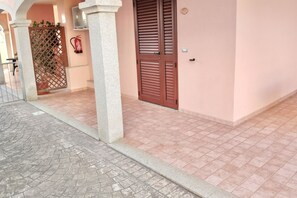 A building entrance with a tiled floor, a wooden door, and a fire extinguisher on the wall. - Cala Gonone, 2-Bedroom Apartment (Cala Gonone)
