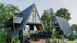 Una casa moderna con techo triangular, un balcón y una hamaca en el patio.