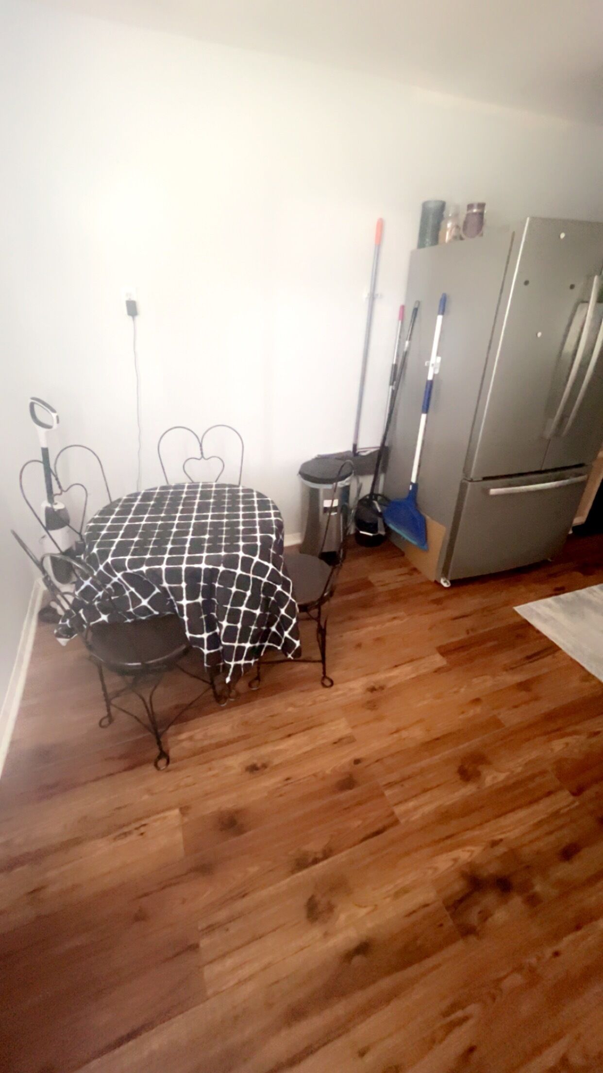 A small kitchen with a dining table, chairs, a refrigerator, and a vacuum cleaner.