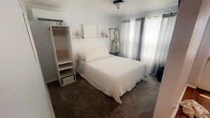 A bedroom with a bed, a wardrobe, a small table, and a window with curtains. - Gorgeous 1-bedroom building with AC in friendly Seymour keypad entry (Seymour)