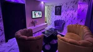 A room with a TV, two armchairs, a sofa, a marble wall, and a door. - Desami Hotel (Lagos)