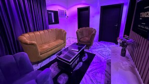 A room with a sofa, armchair, and a small table with a remote control. - Desami Hotel (Lagos)