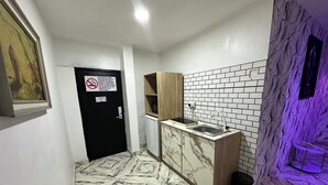 A compact kitchen with a marble floor, a sink, and a black door with a no-smoking sign. - Desami Hotel (Lagos)