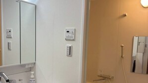 A bathroom with a sink, mirror, towel dispenser, and a shower area with a stool. - YU'S HOUSE 2, a newly built property right next to JR Kamata Station (ootaku)