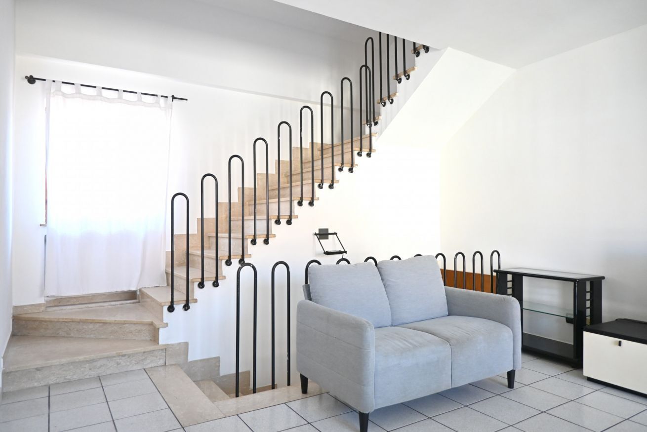 Una escalera con barandilla metálica, un sofá gris y un mueble pequeño.