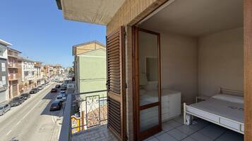 Un balcone con vista sulla strada, una porta scorrevole, un letto e un tavolino.