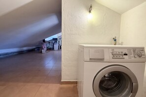 Un cuarto de lavado con lavadora, una lámpara en la pared y vista al área de estar de fondo.