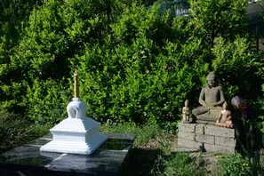 Una statua raffigura una figura seduta su una piattaforma di pietra, circondata da vegetazione lussureggiante.