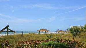 Ein Strand mit Holzgazebos, einem klaren Himmel und einem Gebäude im Hintergrund.