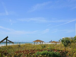 Ein Strand mit Holzgazebos, einem klaren Himmel und einem Gebäude im Hintergrund.