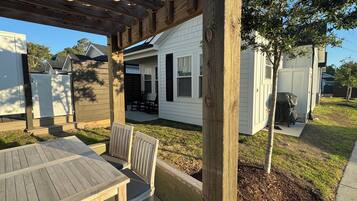 A wooden deck with a table and chairs, a covered grill, and a house with a covered patio.