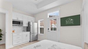 Moderni hotellihuone, jossa on pieni keittiönurkkaus, valkoisilla lakanoilla varustettu sänky ja näkymä ulos.